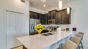 A modern kitchen with dark cabinets, a white countertop, and a bar area with stools. - 9 Mi to Disney Championsgate Condo Plus Water Park (Davenport)
