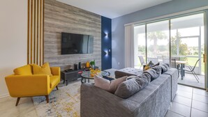 A modern living room with a sofa, armchair, and a flat-screen TV mounted on the wall. - 9 Mi to Disney Championsgate Condo Plus Water Park (Davenport)