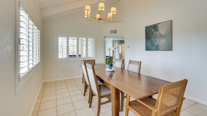 A dining area with a wooden table, six chairs, a chandelier, a window with blinds, and a painting on the wall. - Golf Course Retreat: Pool, Rv/boat Pkg, Lake Views (Lake Havasu City)