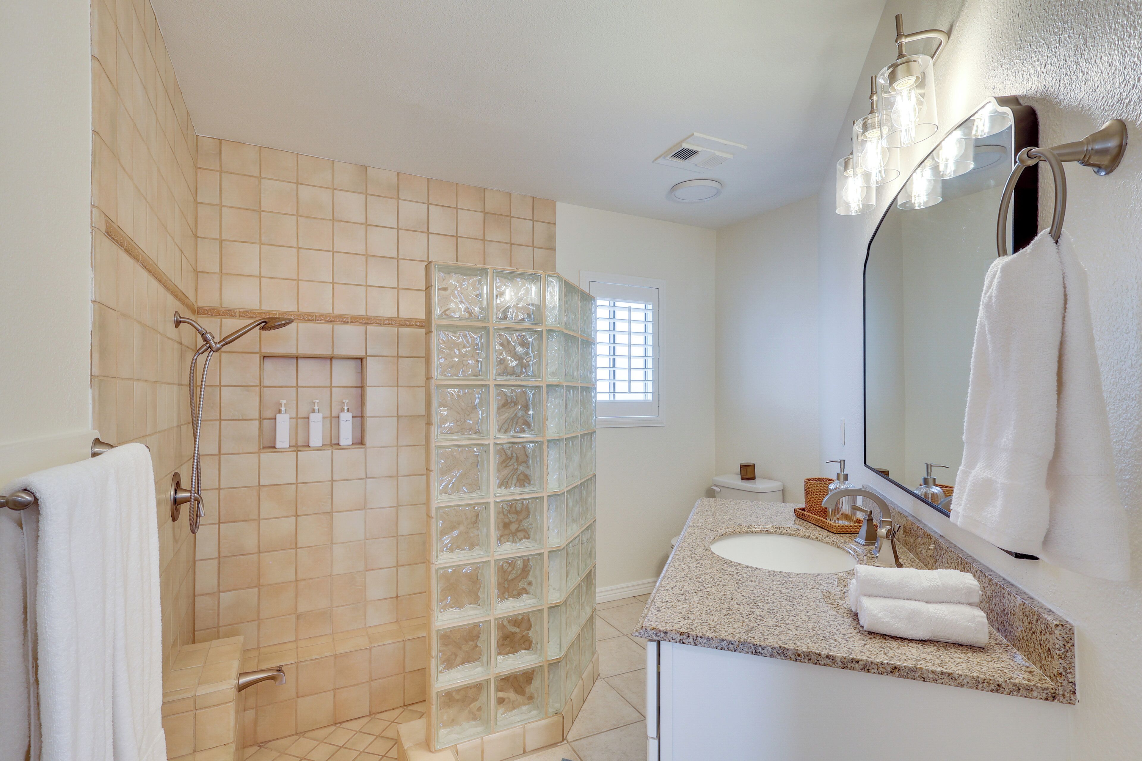 A bathroom with a glass shower enclosure, a sink with a mirror, and a window providing natural light.