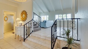 A staircase with black railings, a white wall with a sunburst mirror, and a blue sofa in the background. - Golf Course Retreat: Pool, Rv/boat Pkg, Lake Views (Lake Havasu City)