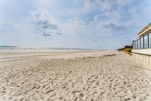 Ein Strand mit einem Gebäude auf der rechten Seite, sandigem Boden und blauem Himmel.