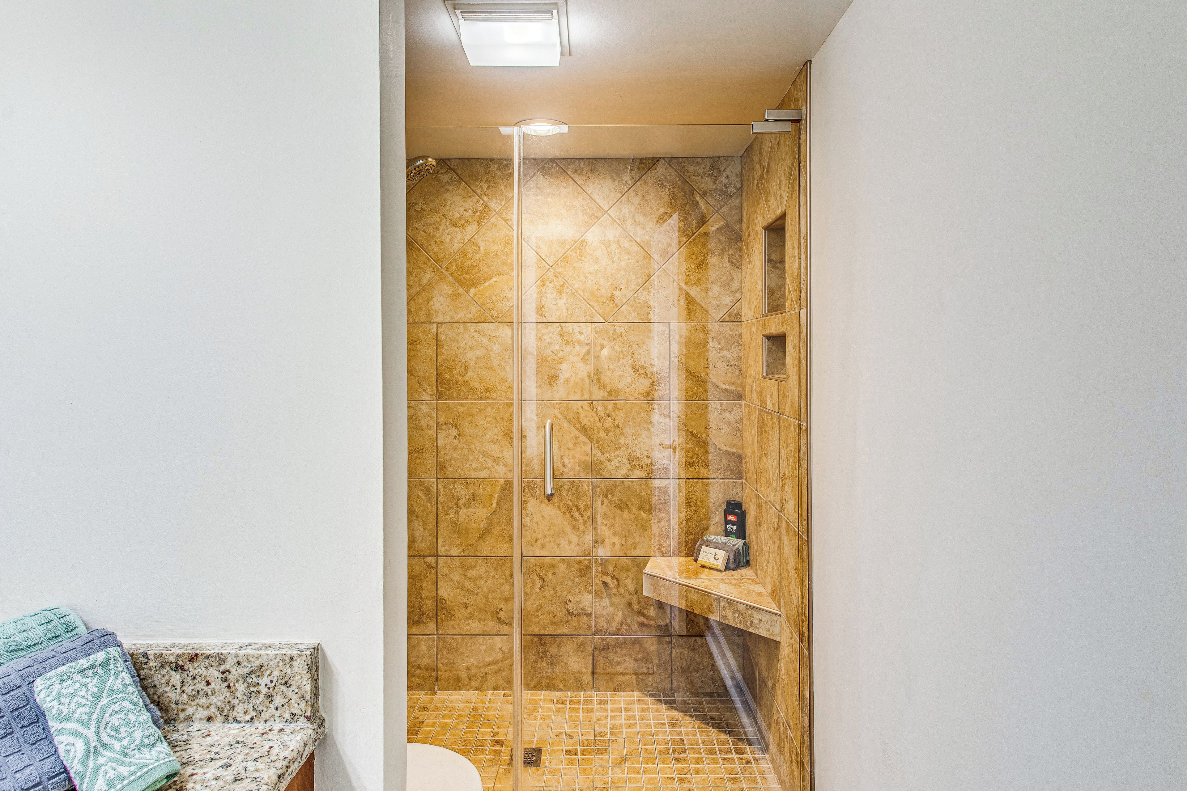 Um chuveiro com porta de vidro, um porta-toalhas e uma prateleira com produtos de higiene pessoal.