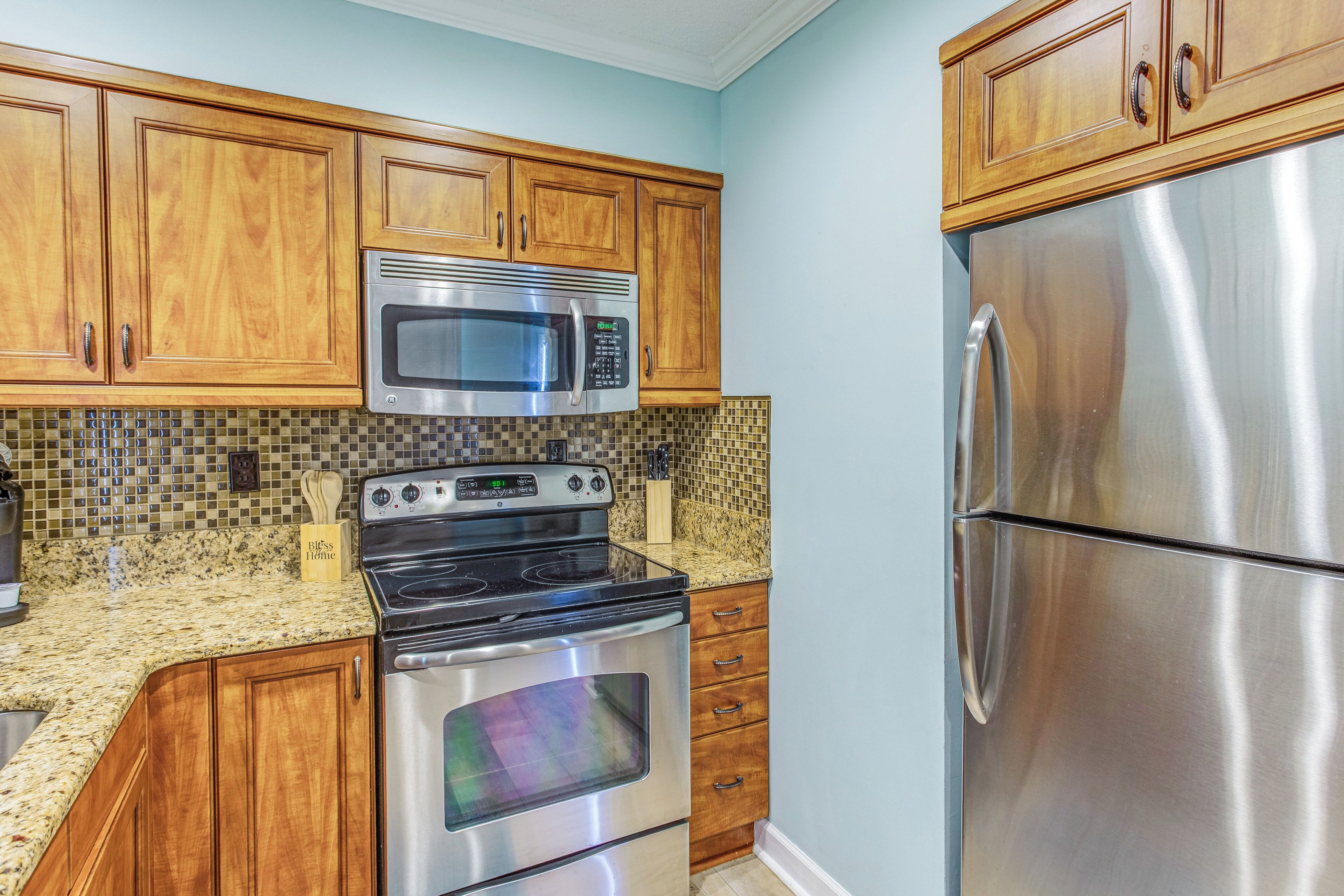 A kitchen with wooden cabinets, a stainless steel refrigerator, a microwave, and an oven.