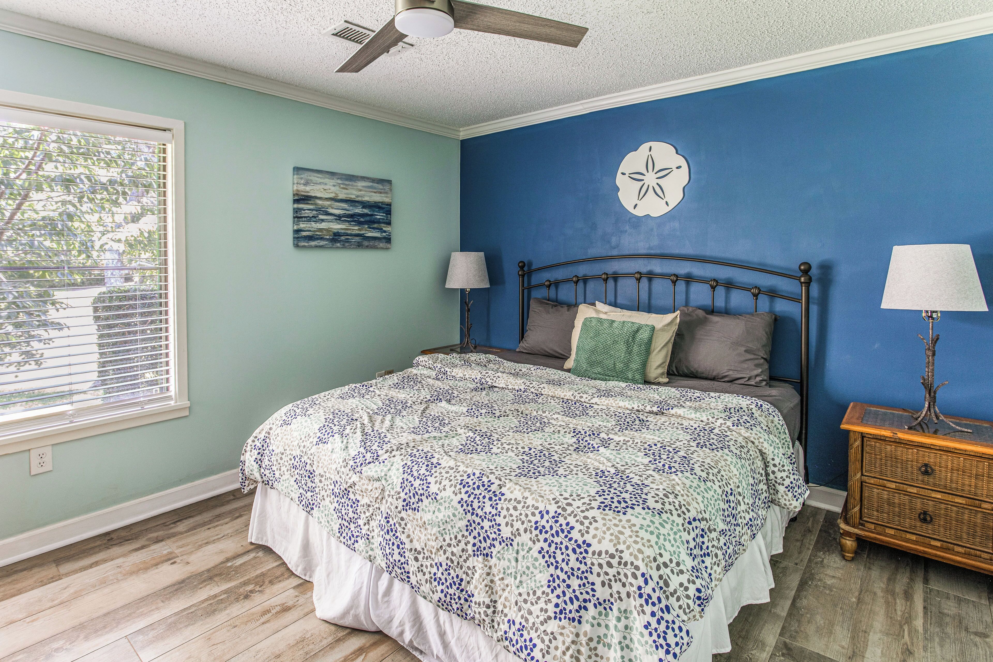 A bedroom with a bed, a nightstand, a wall clock, and a window with blinds.