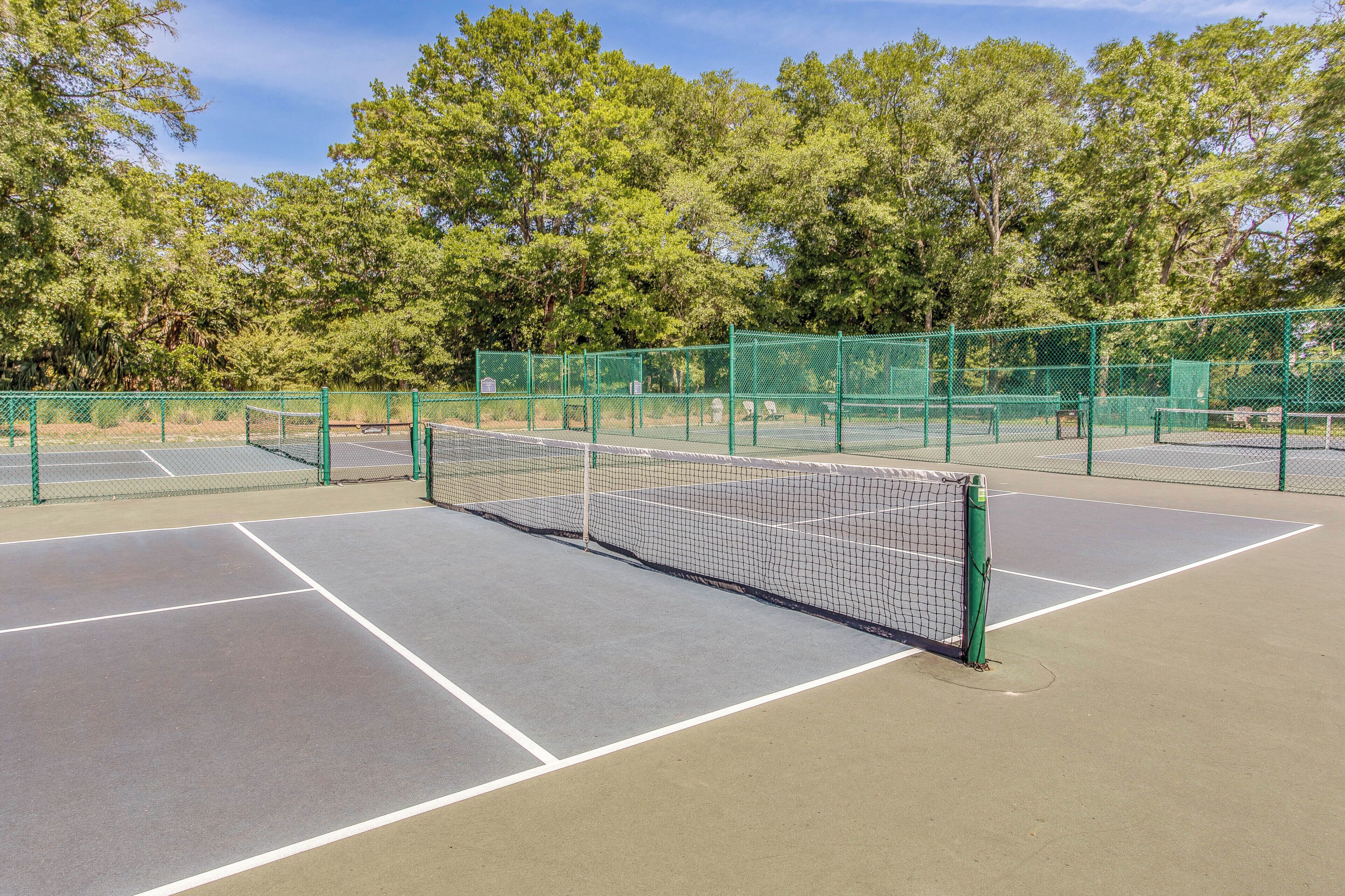 A tennis court with green fencing and a net, surrounded by trees.