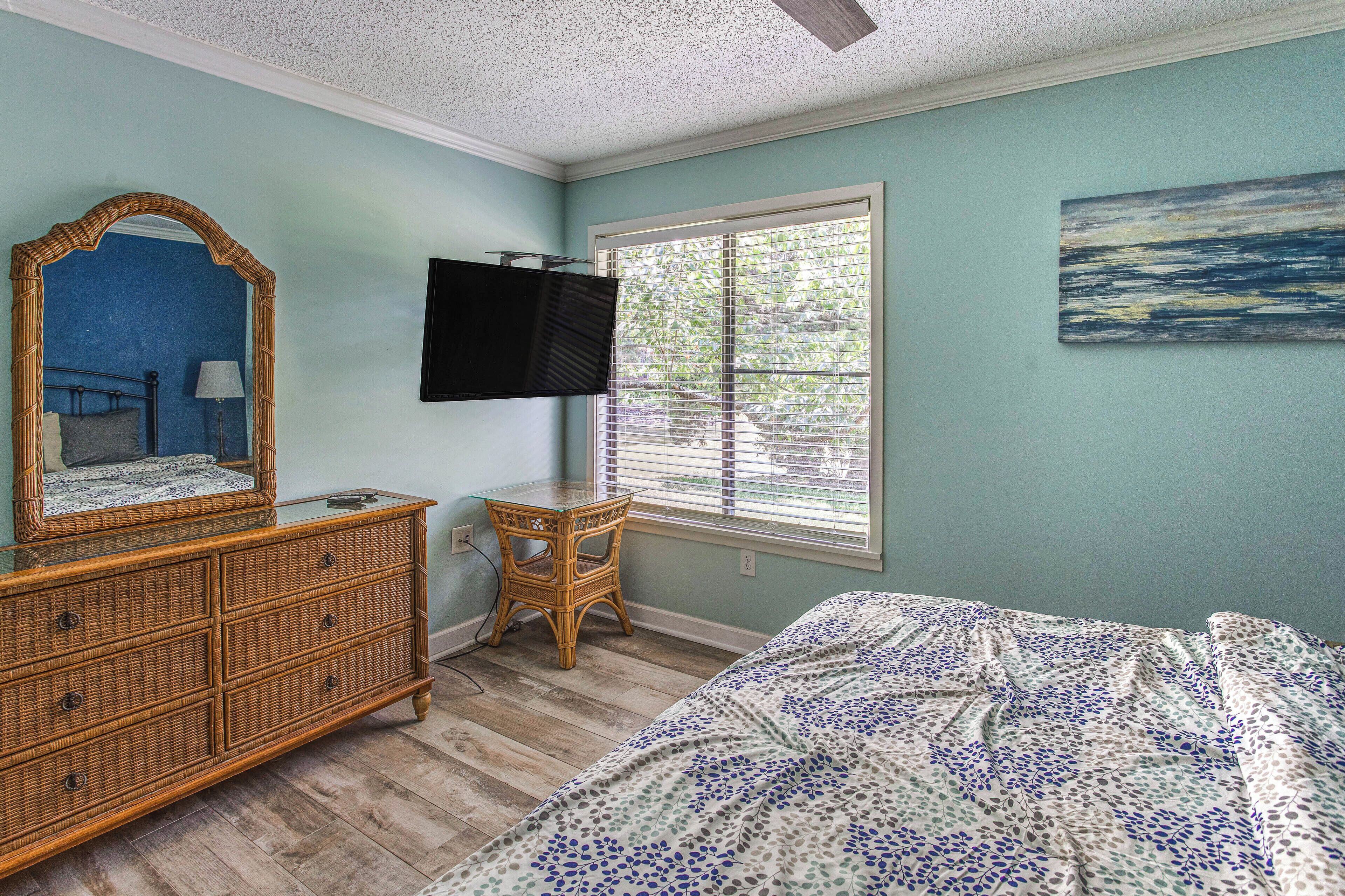 A bedroom with a bed, dresser, television, window, and artwork.