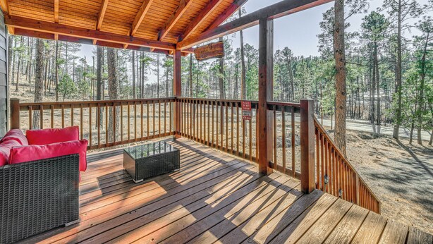 A wooden deck with a covered seating area, a metal table, and a view of a forested area. - Ruidoso Alpine Escape w/ 2 Cabins, Near Alto Lake! (Ruidoso)