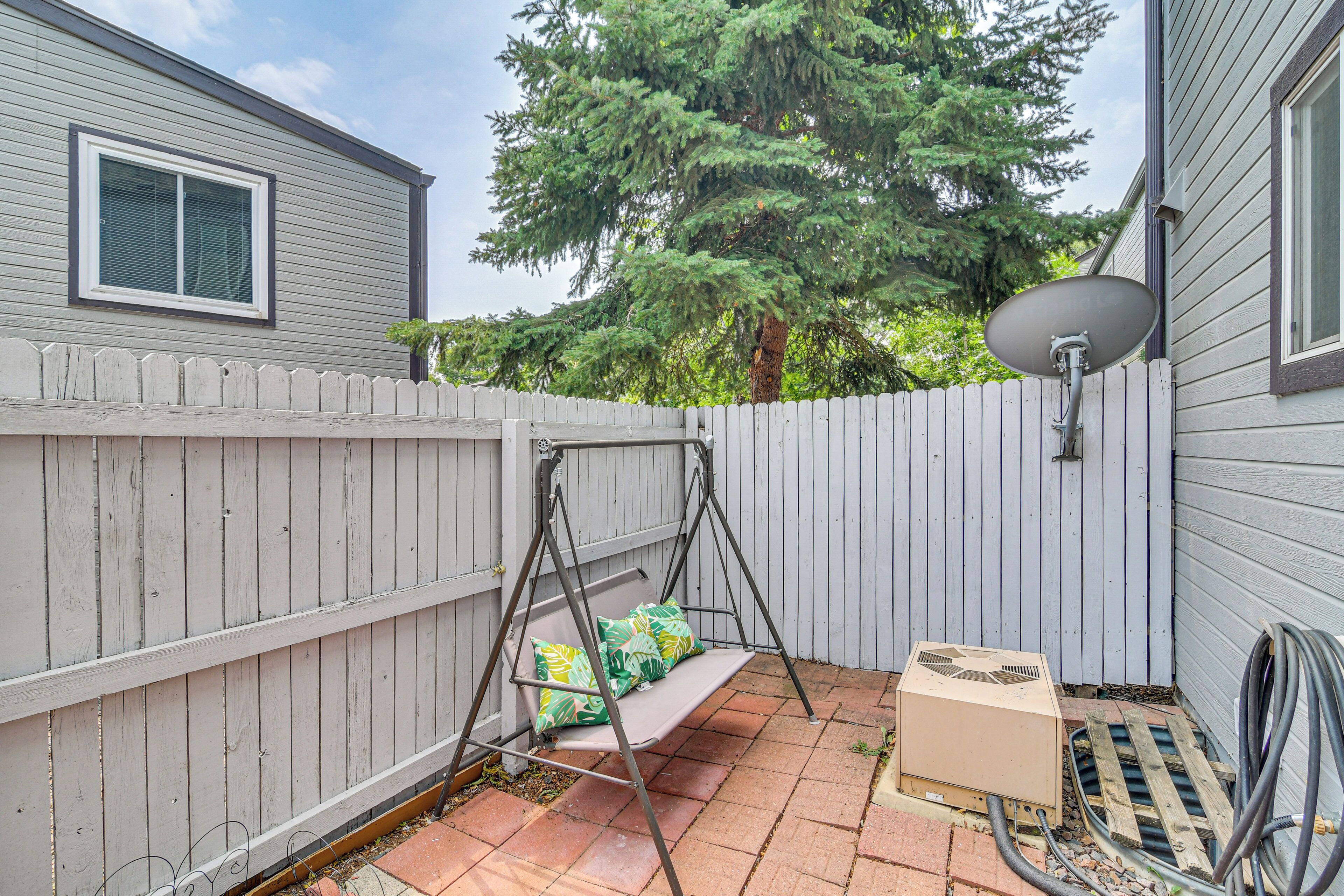 A backyard with a white picket fence, a swing, a satellite dish, and a portable heater.