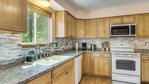 A kitchen with wooden cabinets, a granite countertop, a built-in microwave, a stove, and a window with blinds. - 3 Mi to Old Town Arvada! Family Townhome w/ Patio (Arvada)
