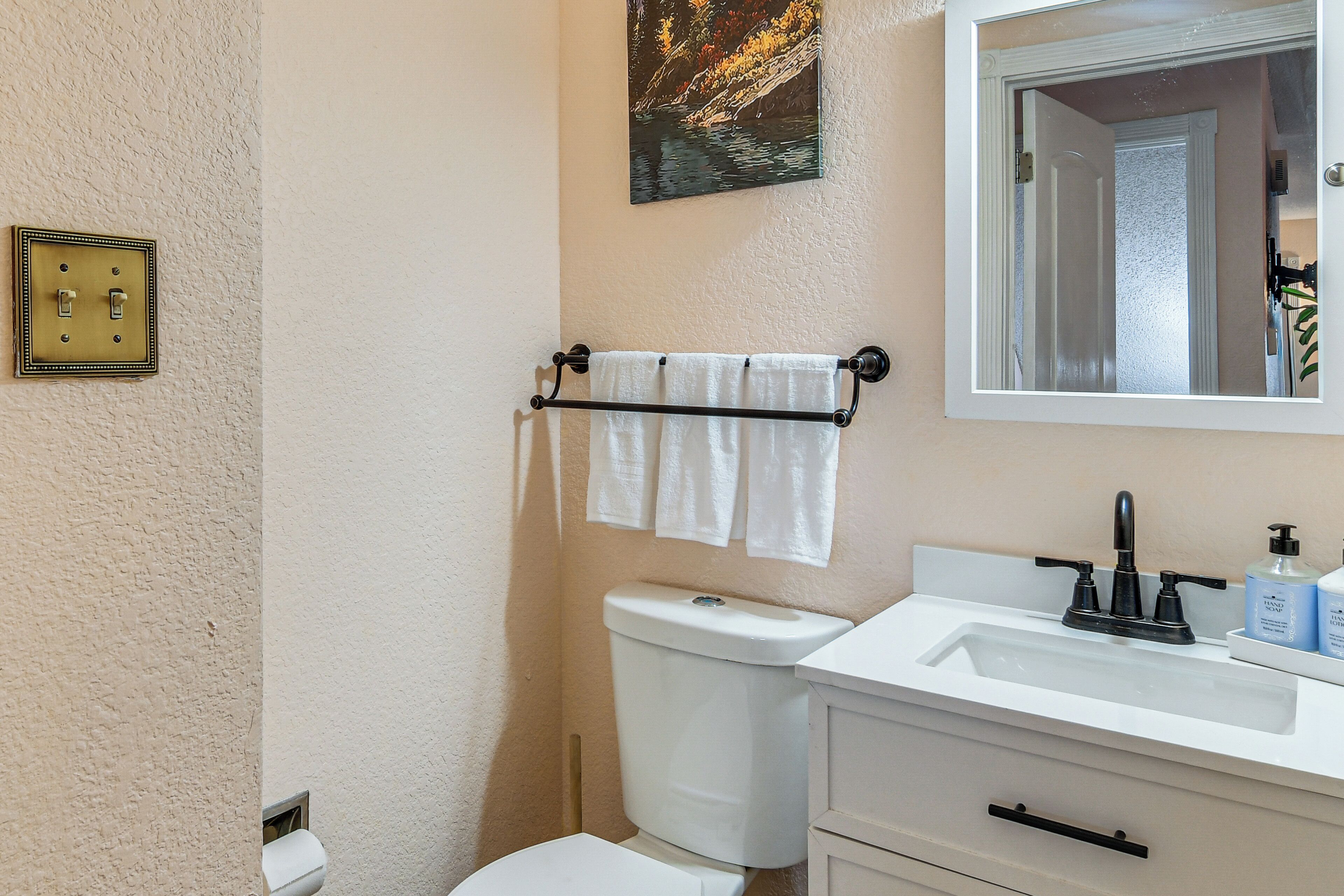 A bathroom with a toilet, sink, towel rack, and a painting on the wall.