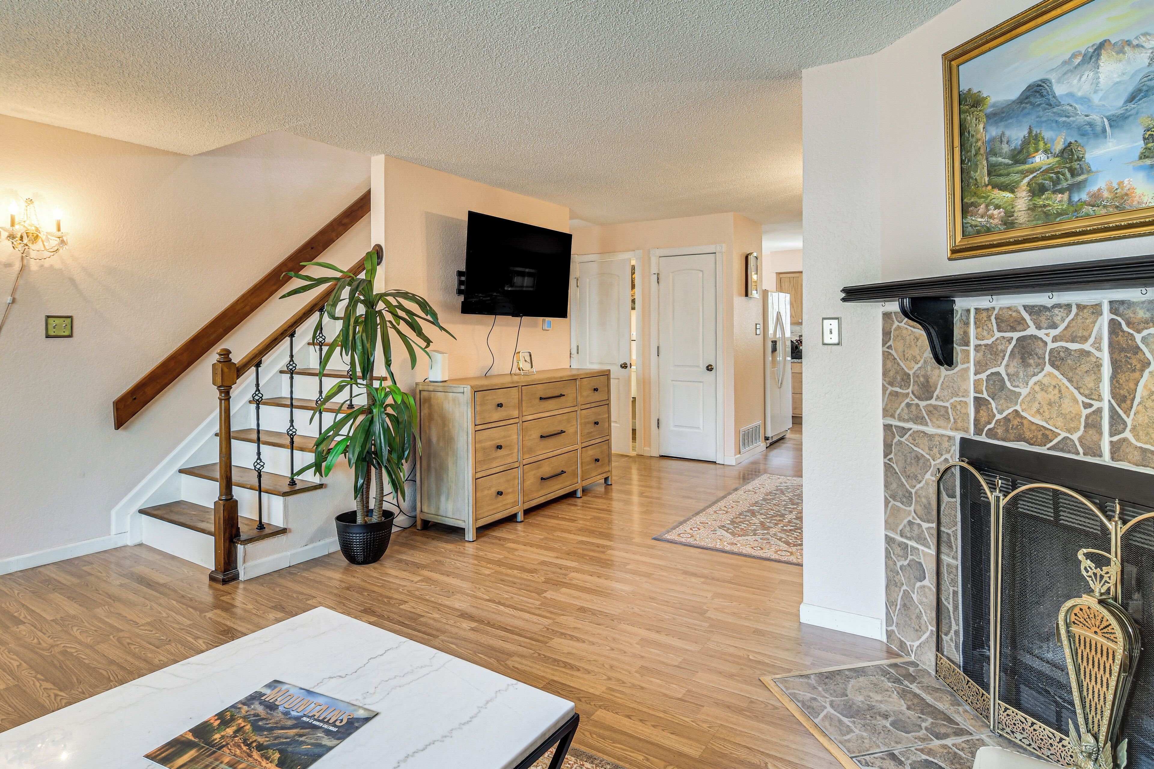 A living room with hardwood floors, a fireplace, a staircase, a flat-screen TV, and a dining area.
