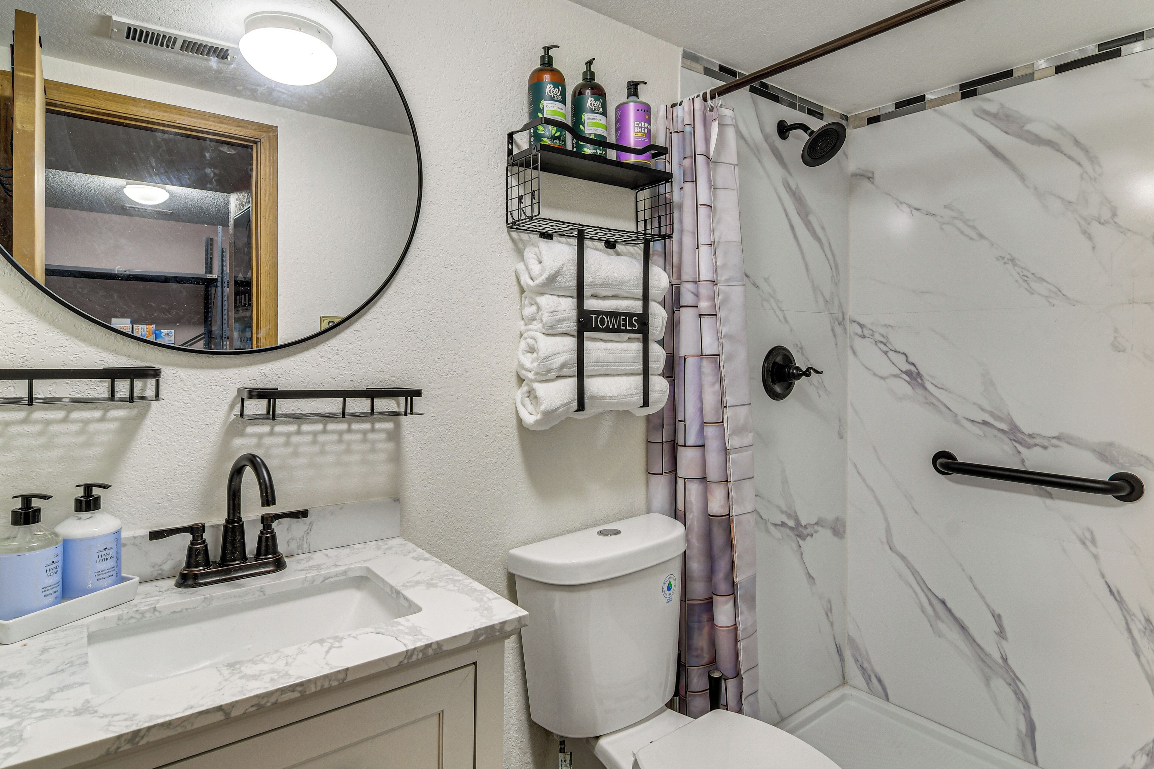 A bathroom with a marble sink, a toilet, a shower with a curtain, and a shelf with toiletries.
