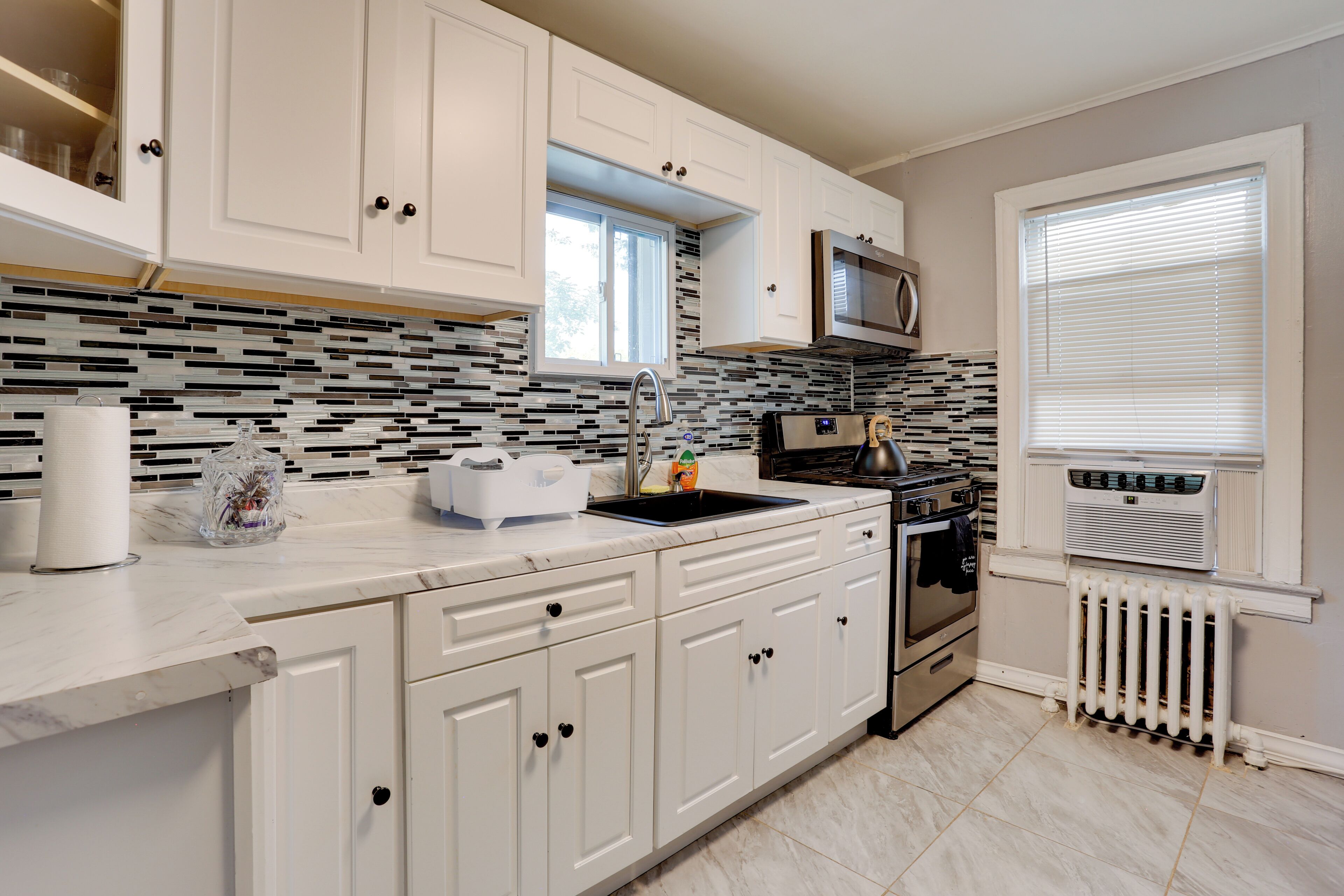 A modern kitchen with white cabinets, a black and white backsplash, a stainless steel sink, and a built-in microwave.