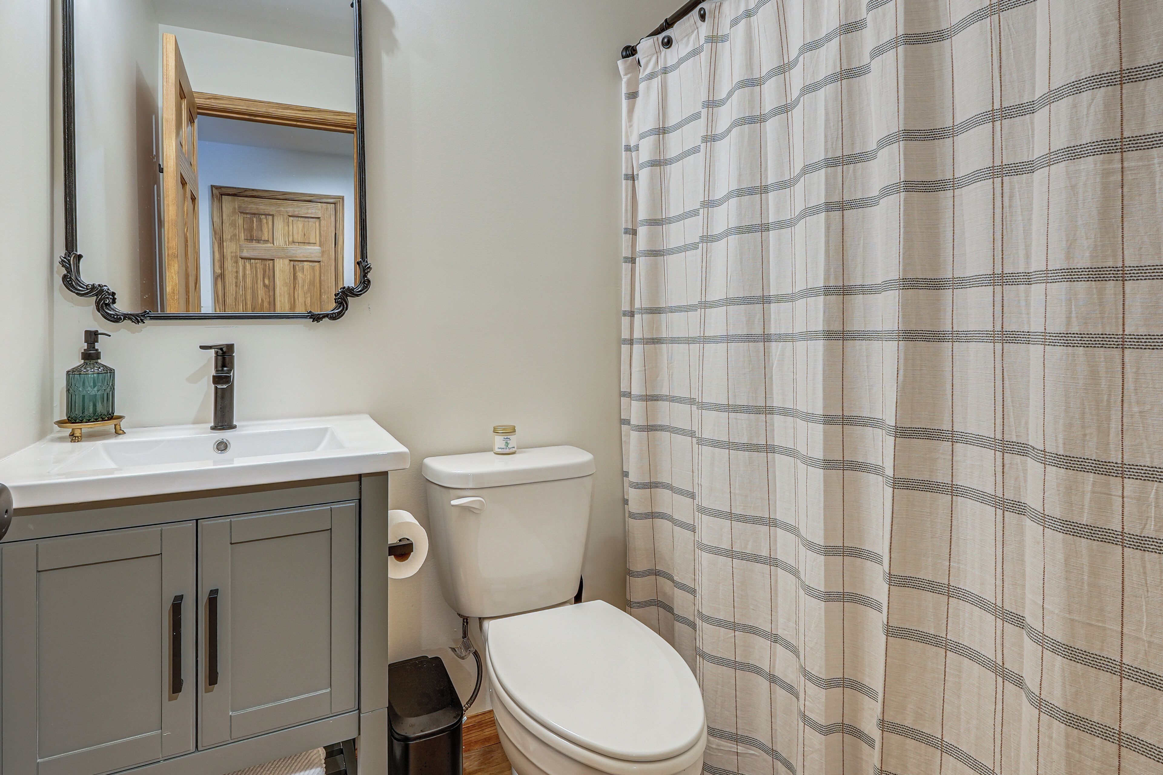 A bathroom with a toilet, sink, mirror, and shower curtain.