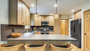 A modern kitchen with wooden cabinets, a large island with bar stools, a black refrigerator, and pendant lighting. - 1 Mi to Beach! Home w/ Game Room in Albrightsville (Albrightsville)