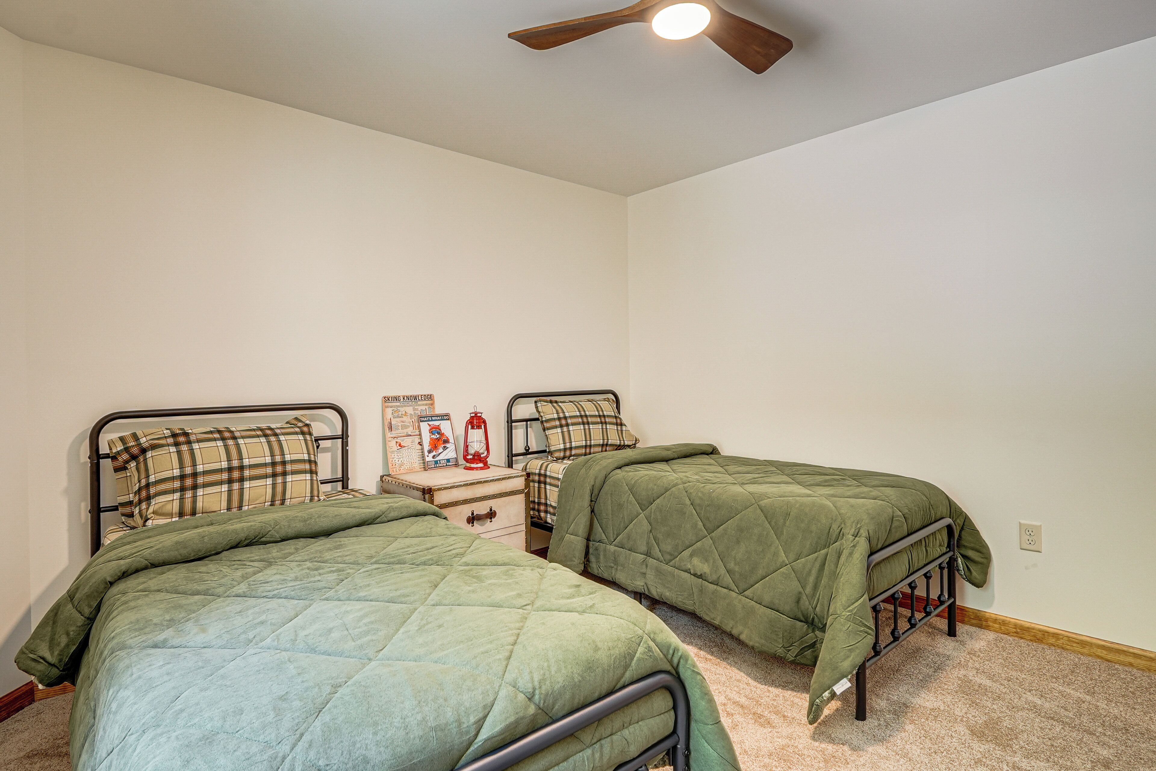 A bedroom with two twin beds, a nightstand, a lamp, and a ceiling fan.