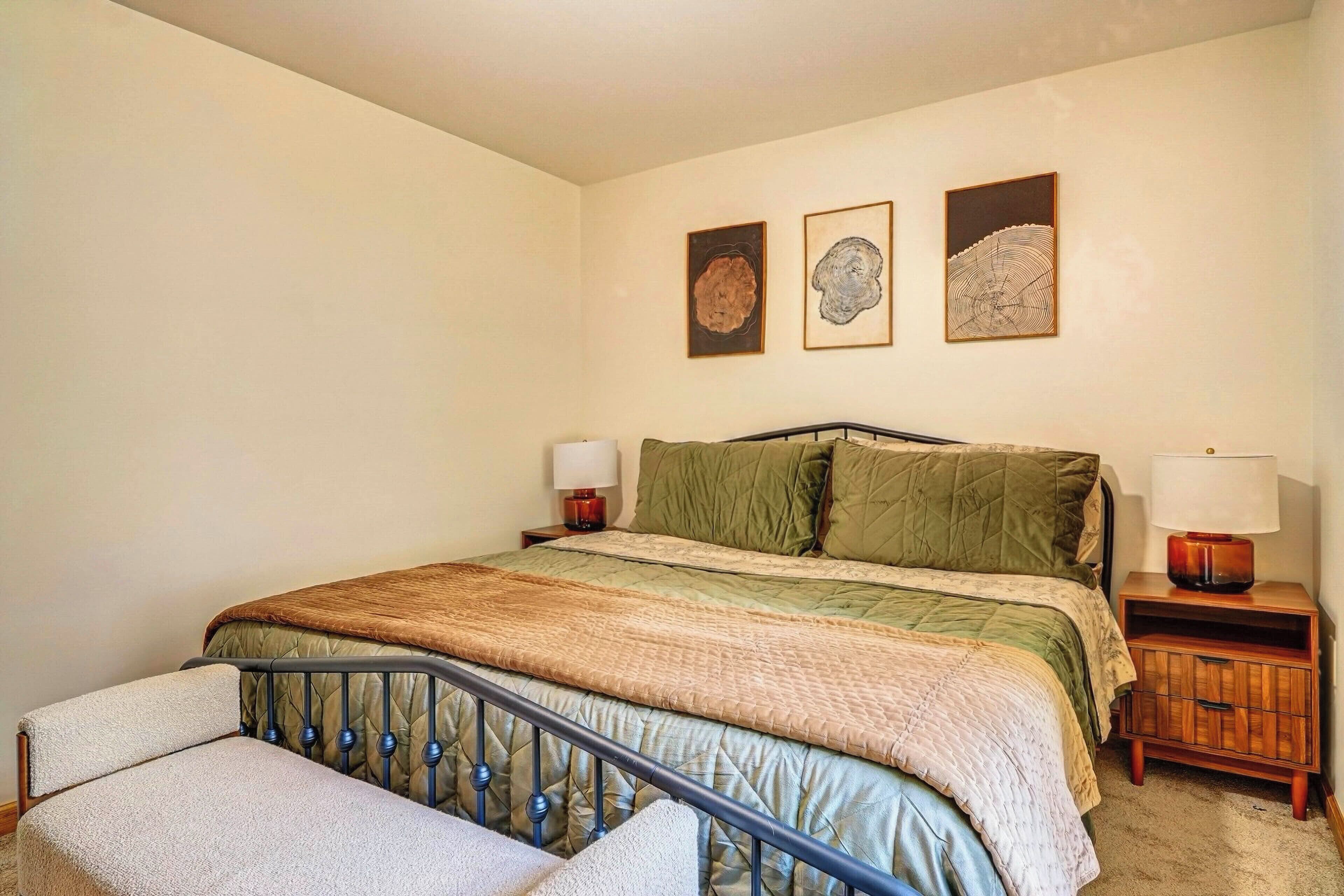 Een slaapkamer met een bed, twee nachtkastjes, een lamp en drie foto’s aan de muur.