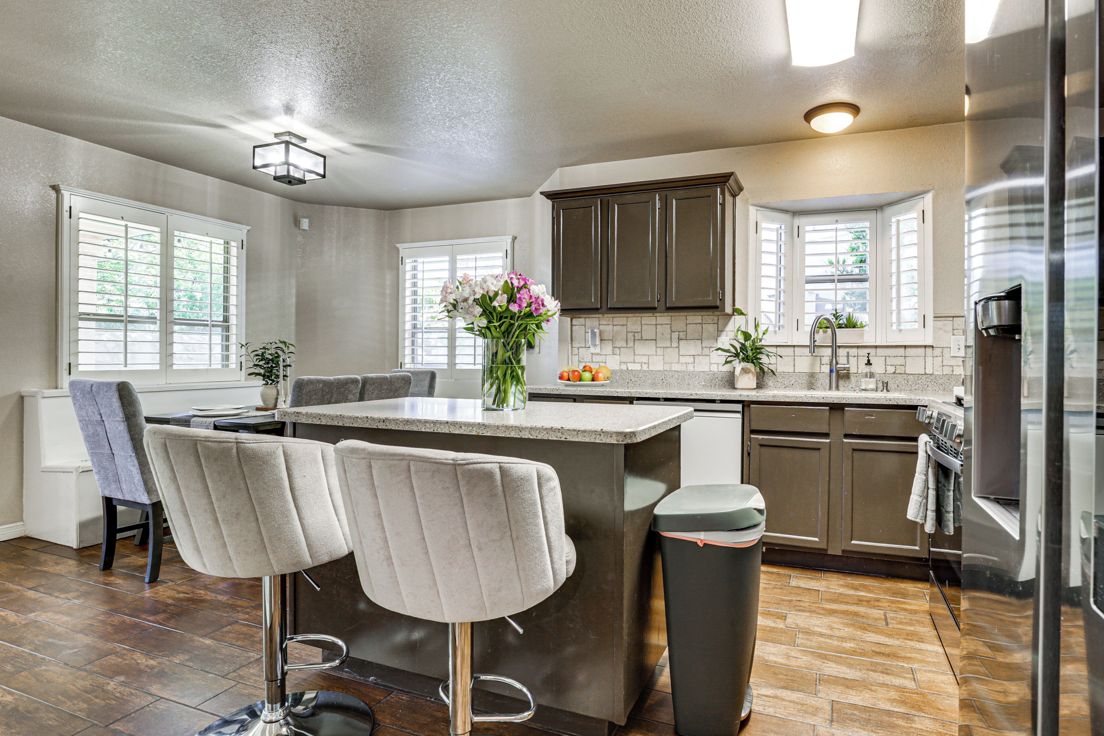 A modern kitchen with a central island, bar stools, a trash can, and a refrigerator.