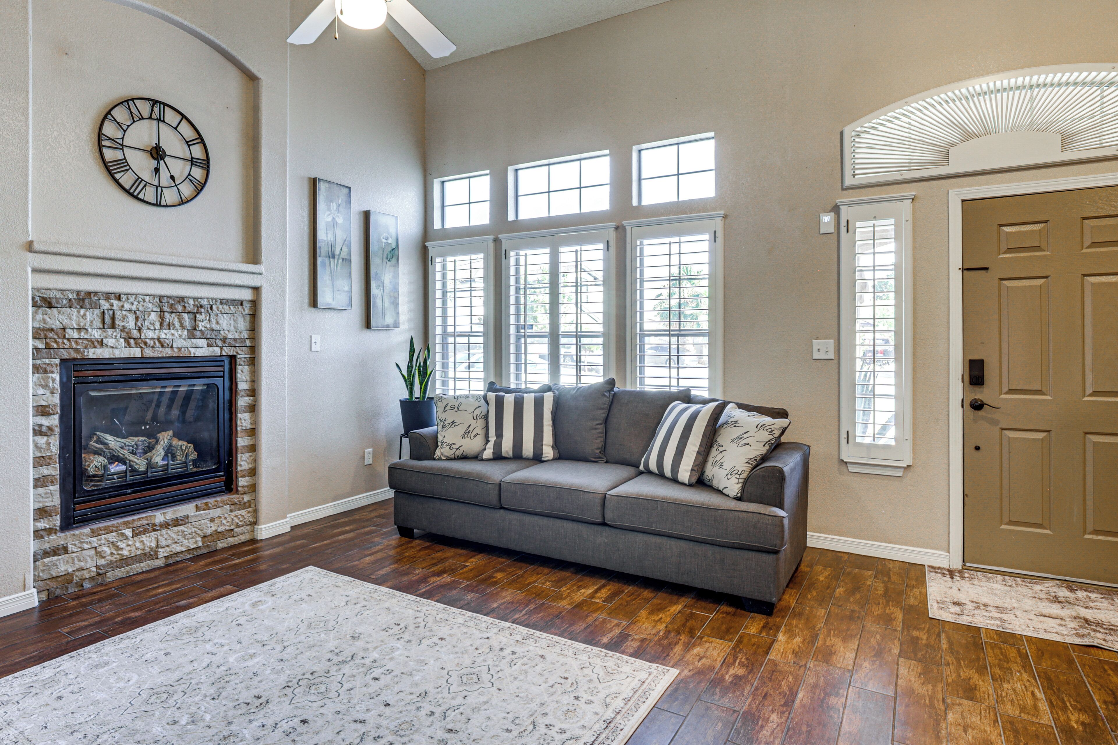 A living room with a fireplace, a sofa with pillows, a clock, and a door.