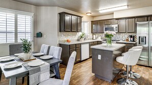 Una cocina moderna con armarios oscuros, una isla central y un comedor con una mesa dispuesta para cuatro.