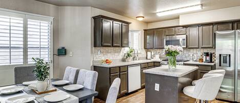 Una cocina moderna con armarios oscuros, una isla central y un comedor con una mesa dispuesta para cuatro.