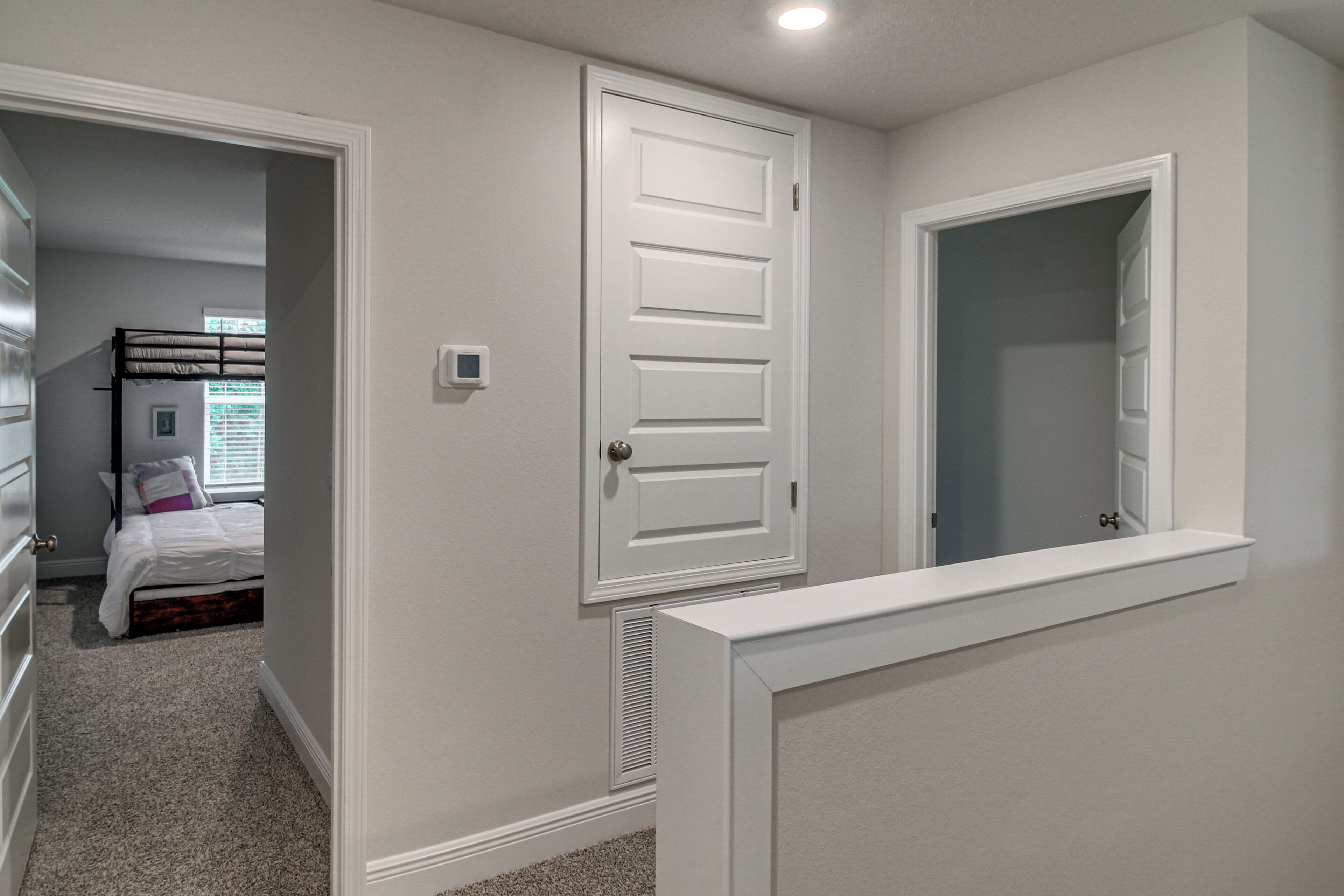 A bedroom with a bed, a door, a mirror, and a carpeted floor.
