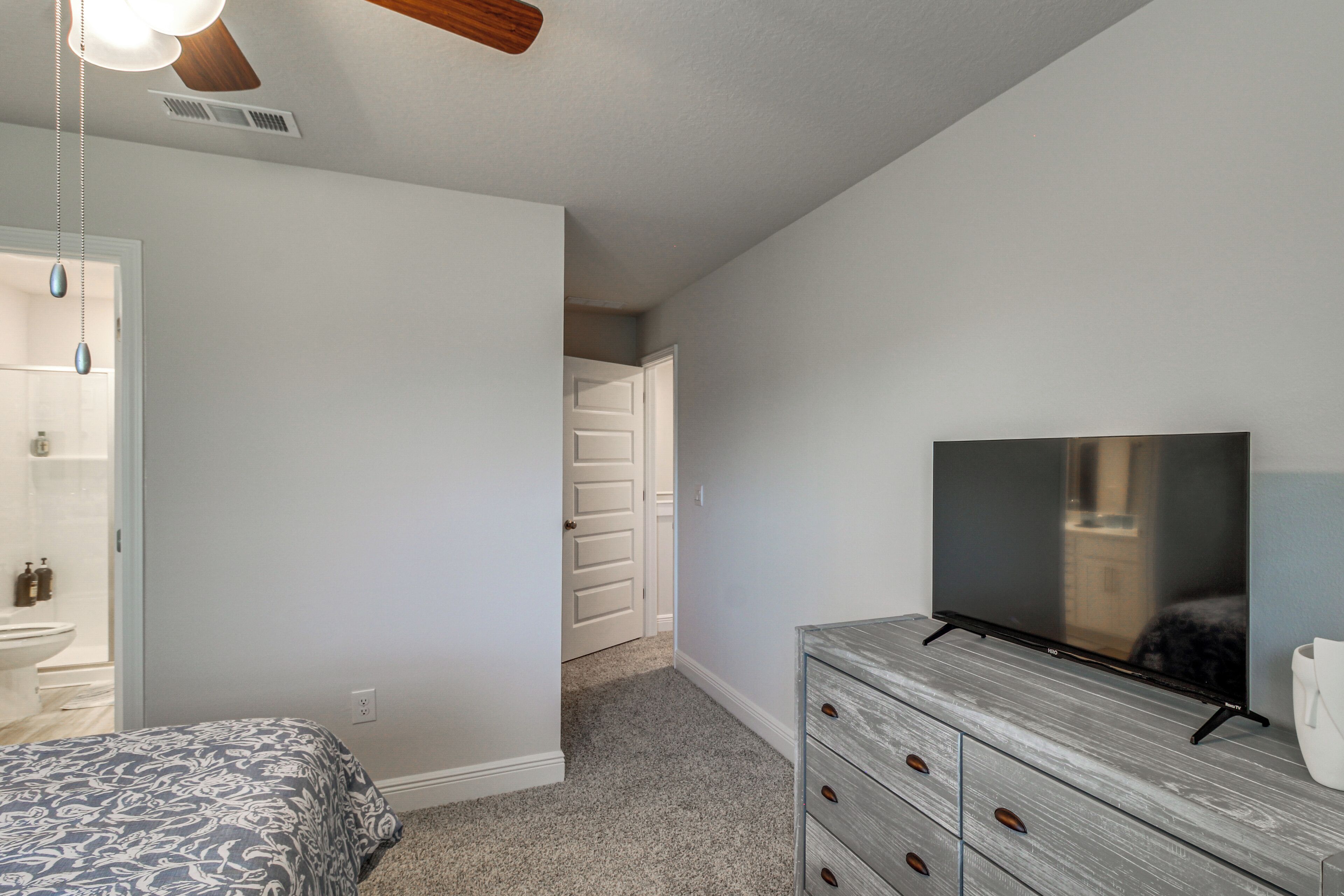 A bedroom with a bed, a dresser, a television, and a door leading to a bathroom.