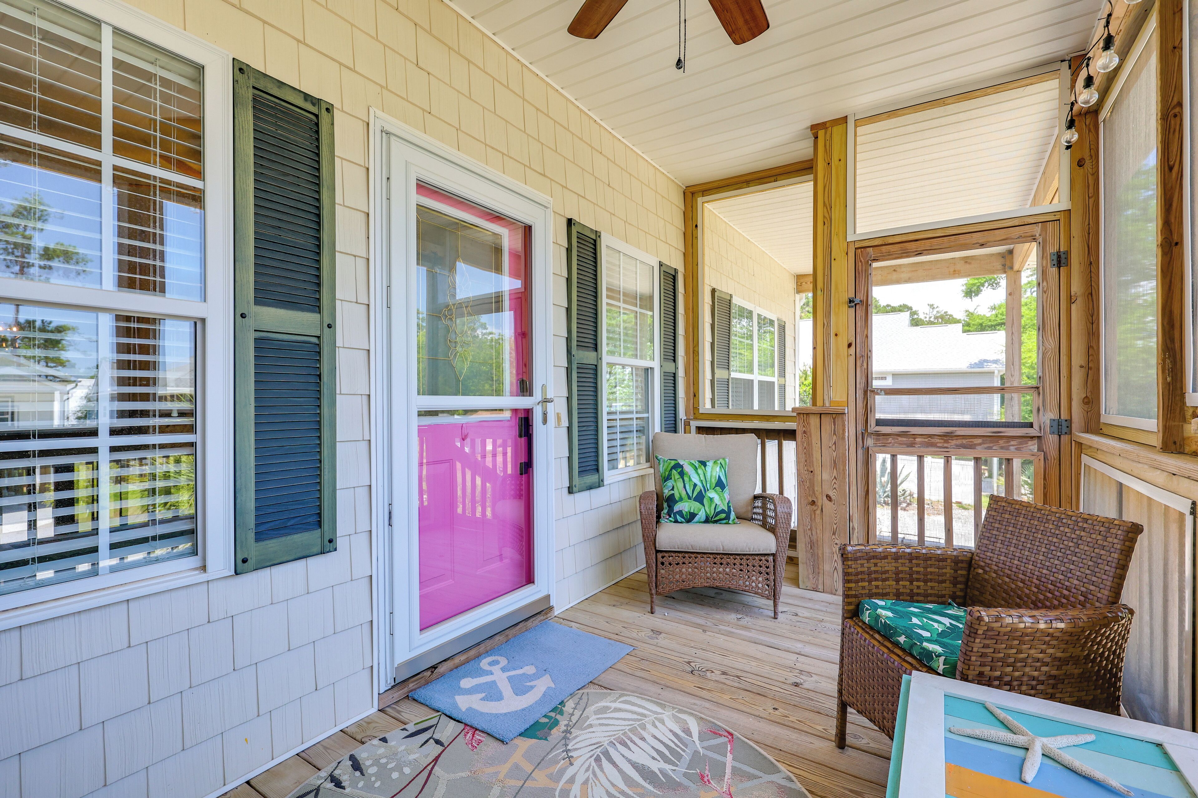 A covered porch with a wicker chair, a door with a pink frame, and a wooden ceiling.