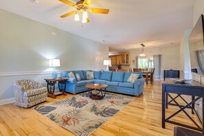 A living room with a blue sofa, patterned armchair, wooden coffee table, and a large rug. - Golf Cart, Bikes, Easy Beach Days! Oak Island (Oak Island)