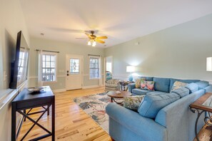 A living room with a blue sofa, a coffee table, a TV, and a ceiling fan. - Golf Cart, Bikes, Easy Beach Days! Oak Island (Oak Island)