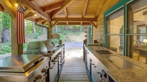 Una cabaña de madera con espacio de cocina que incluye una parrilla, un lavamanos y vistas al bosque.