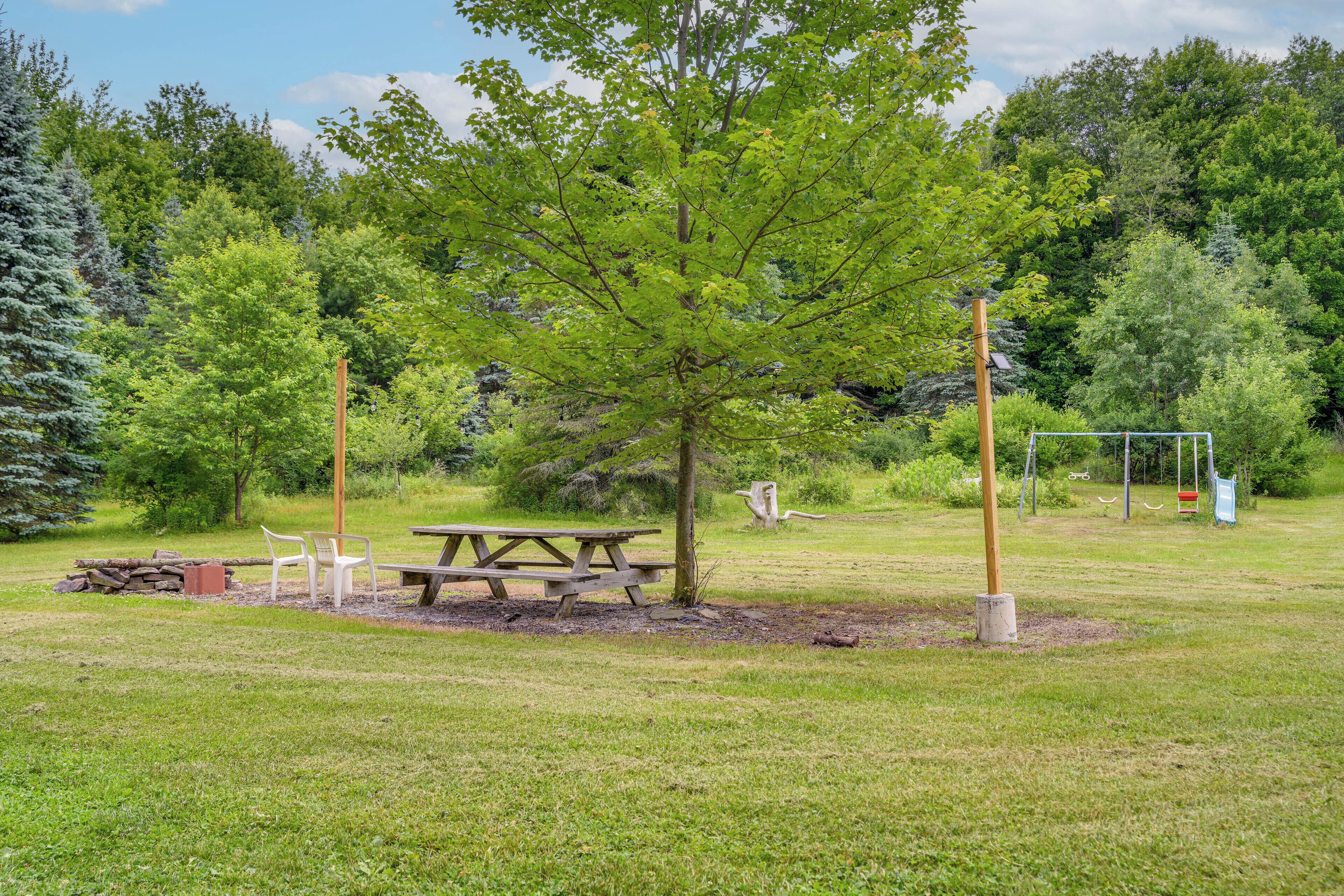 A picnic area with a table and chairs, surrounded by trees and a swing set.