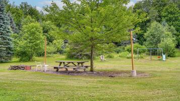 A picnic area with a table and chairs, surrounded by trees and a swing set.