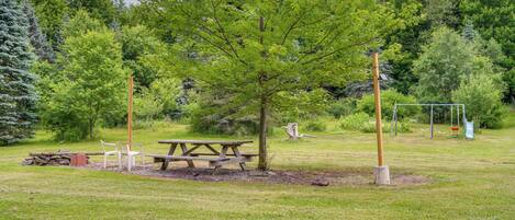 A picnic area with a table and chairs, surrounded by trees and a swing set.