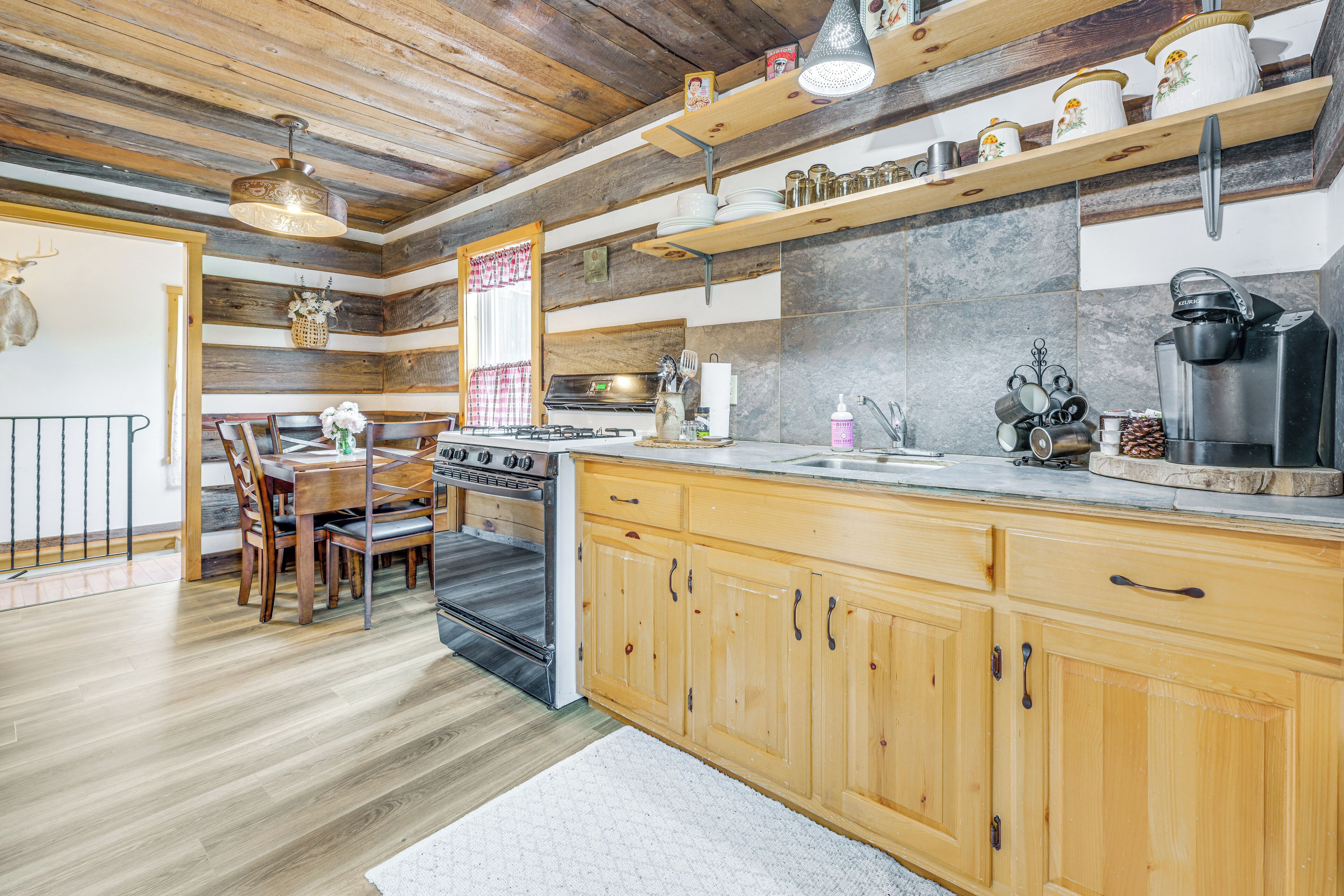 A rustic kitchen with wooden cabinets, a stove, and a dining area with chairs and a table.