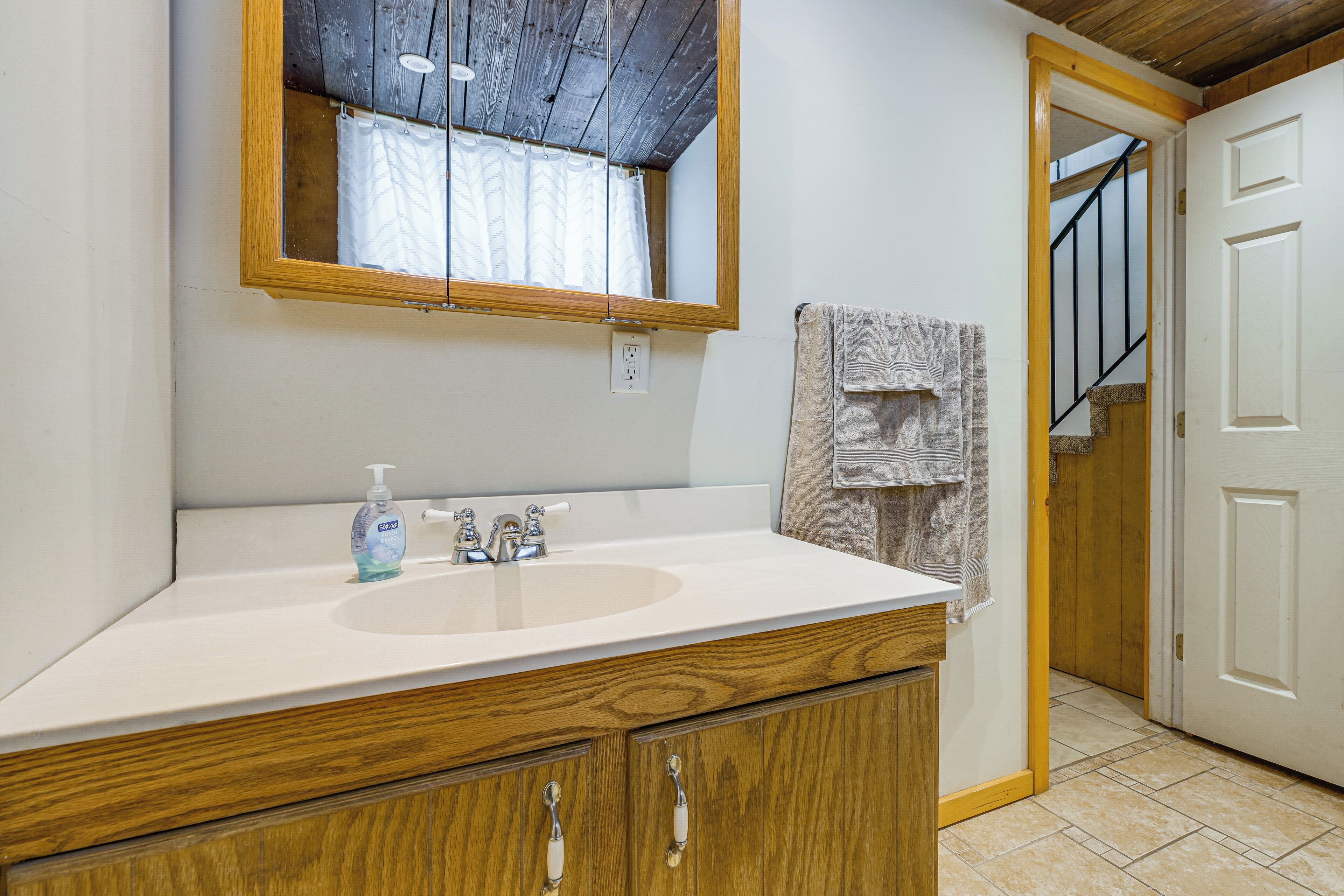 A bathroom with a wooden vanity, a mirror, a sink, and a towel rack.