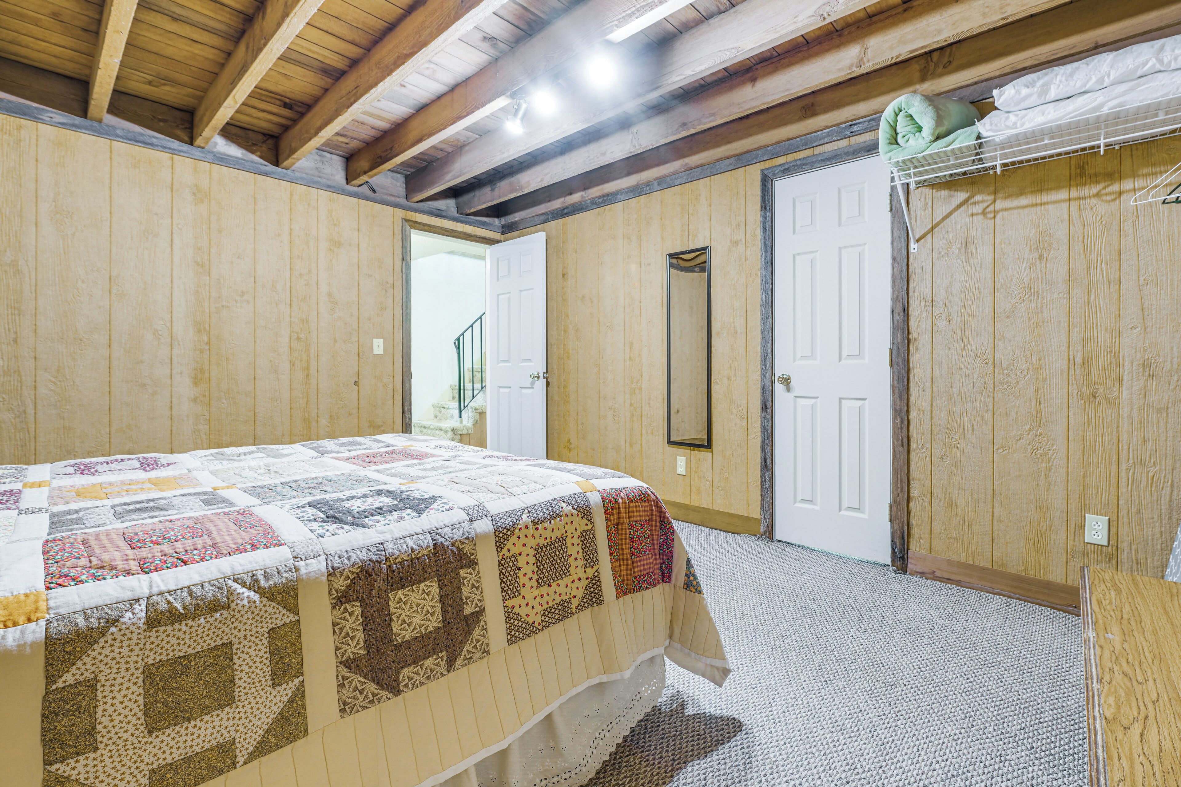 Una camera da letto con una coperta trapuntata, pareti in legno, una porta e uno specchio.