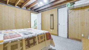 Una camera da letto con una coperta trapuntata, pareti in legno, una porta e uno specchio.