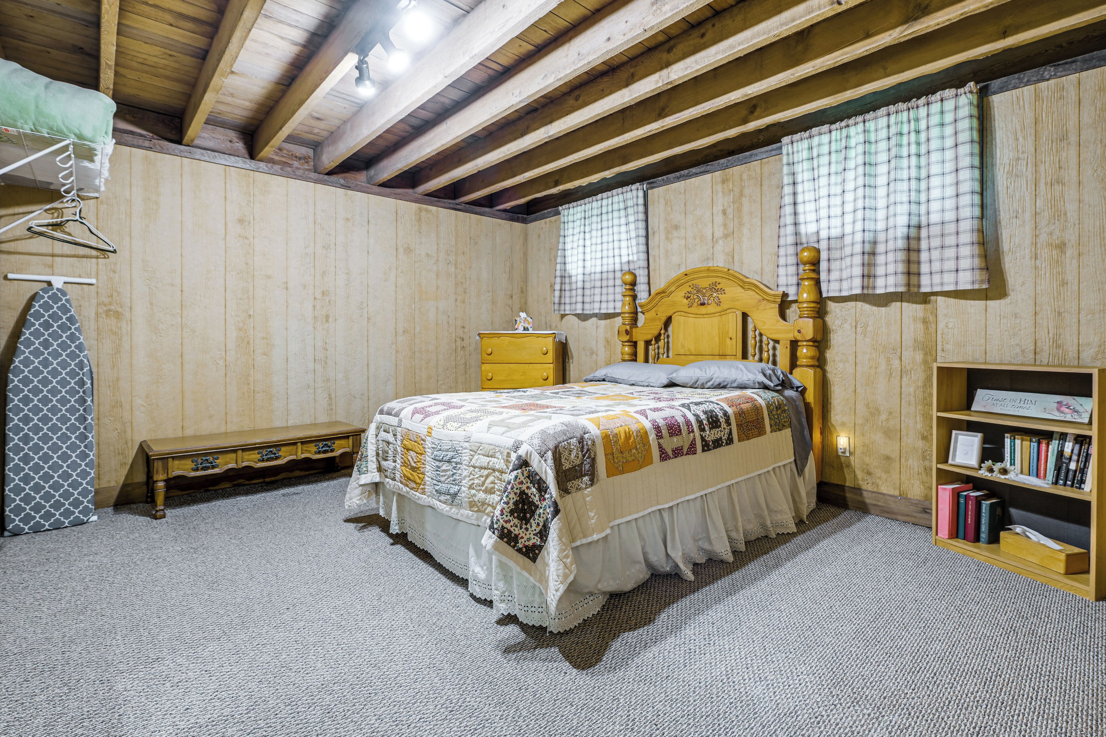 Une chambre à coucher avec un lit en bois, une table de chevet, une bibliothèque et une fenêtre avec des rideaux.