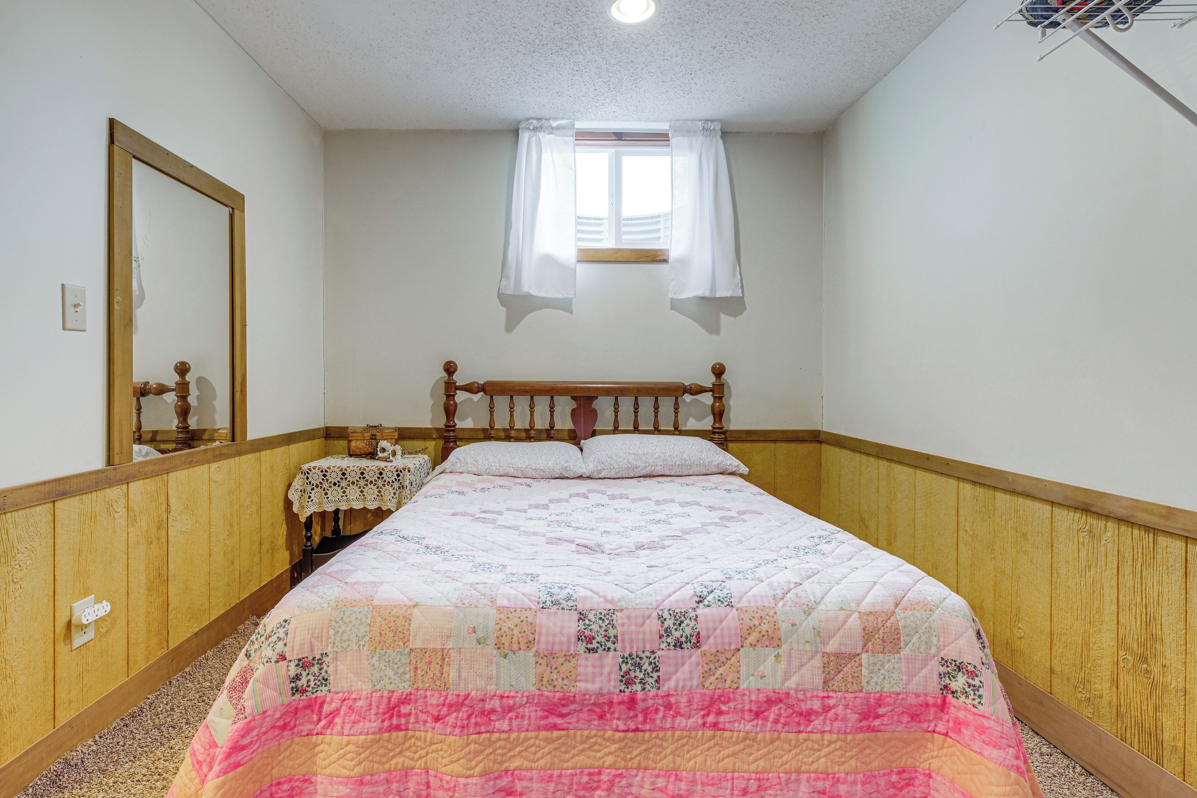 A bedroom with a wooden headboard, a quilted bedspread, a nightstand, a mirror, and a window with curtains.