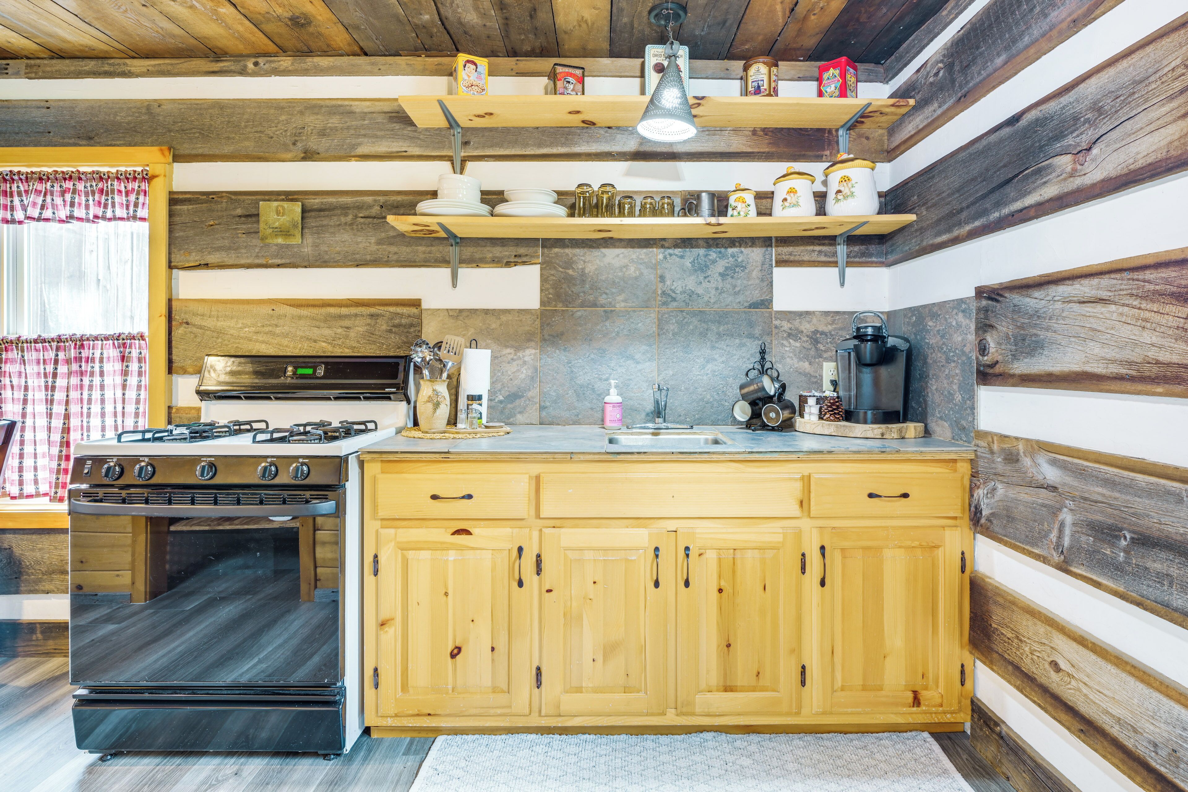 A kitchen with wooden cabinets, a stove, a sink, and shelves with jars and utensils.