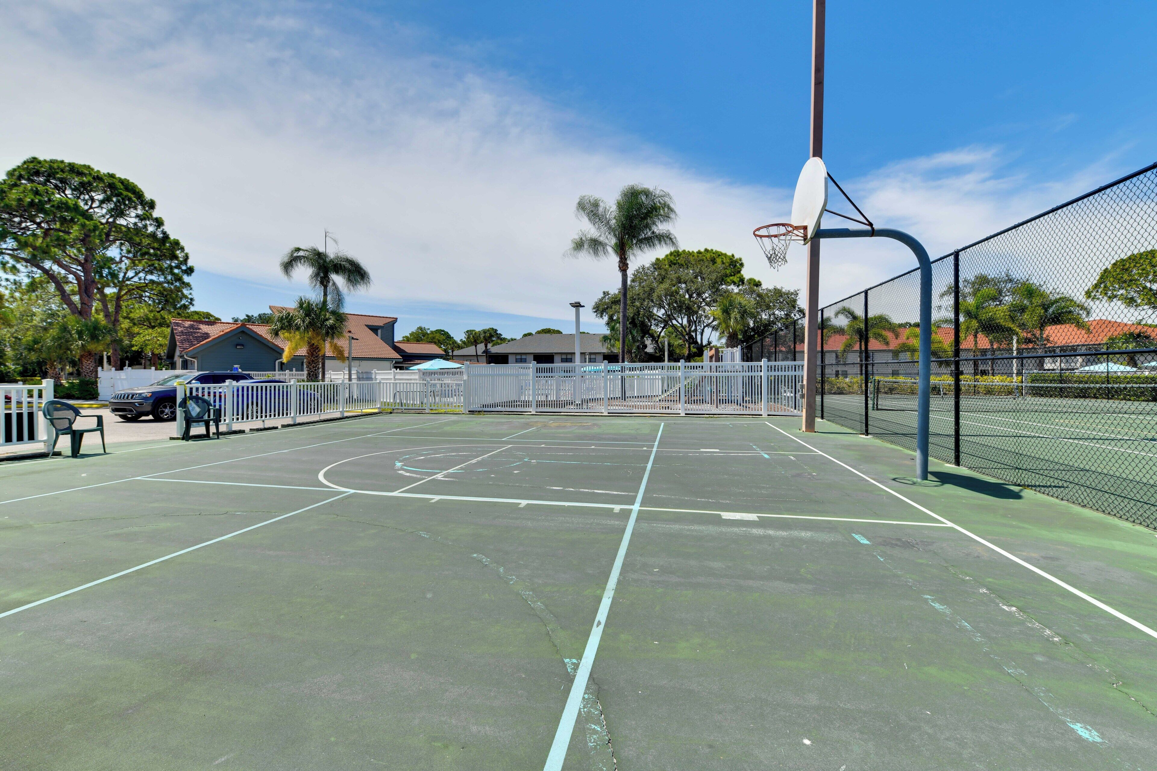 An outdoor basketball court with a net, a fence, and trees in the background.
