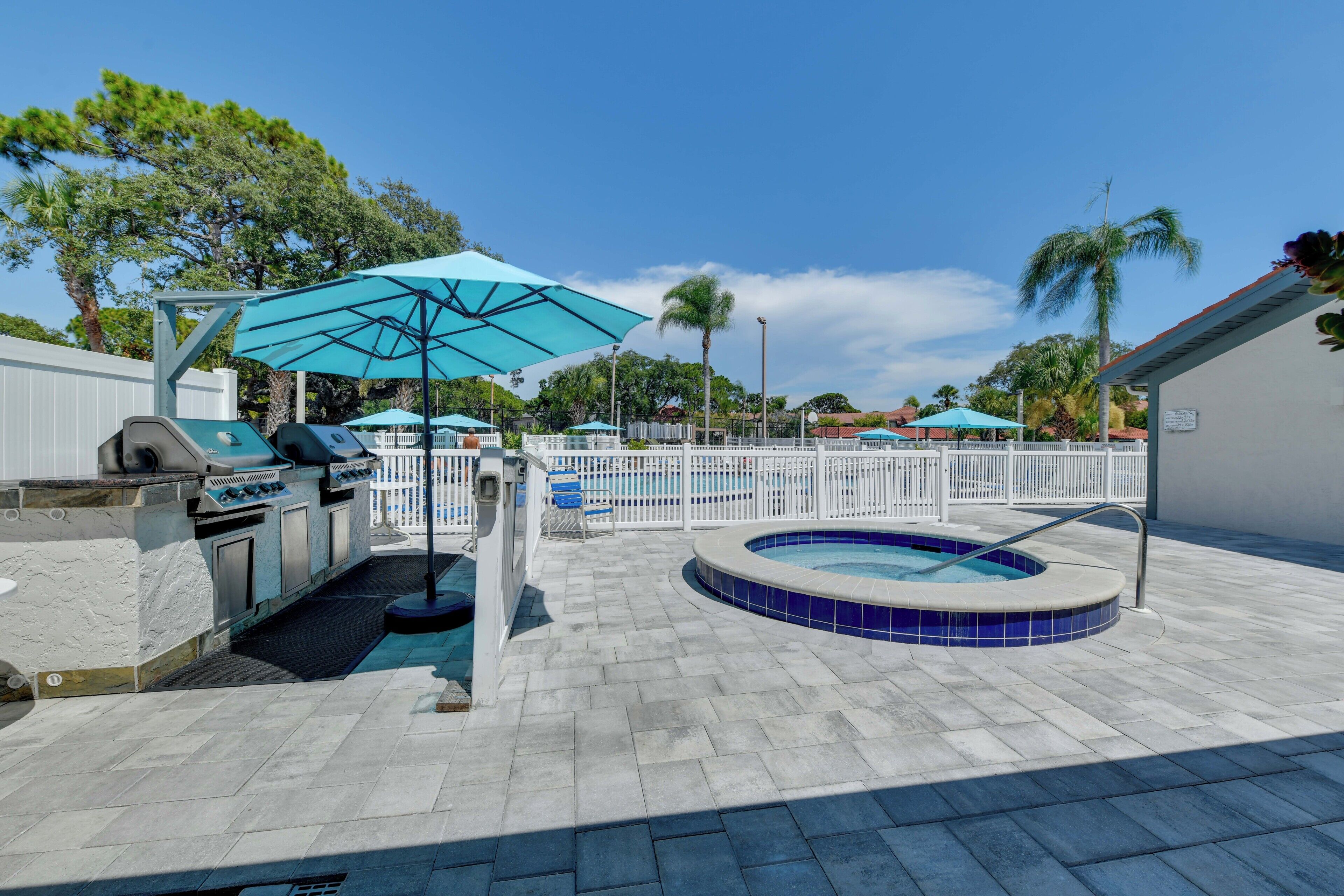 A pool area with a hot tub, barbecue grill, and umbrellas.