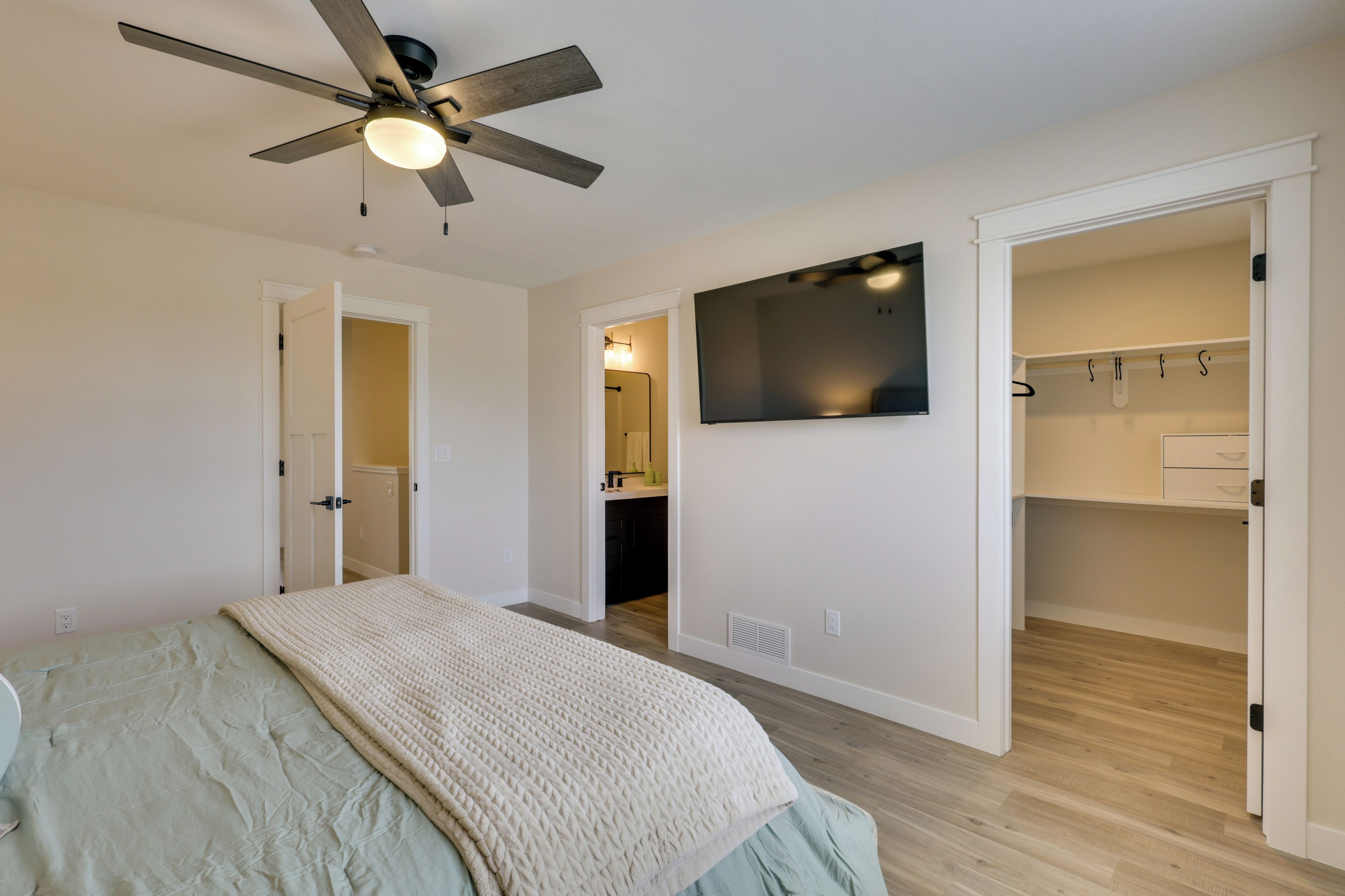 A bedroom with a bed, a ceiling fan, a TV, and an open closet.