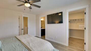 A bedroom with a bed, a ceiling fan, a TV, and an open closet.