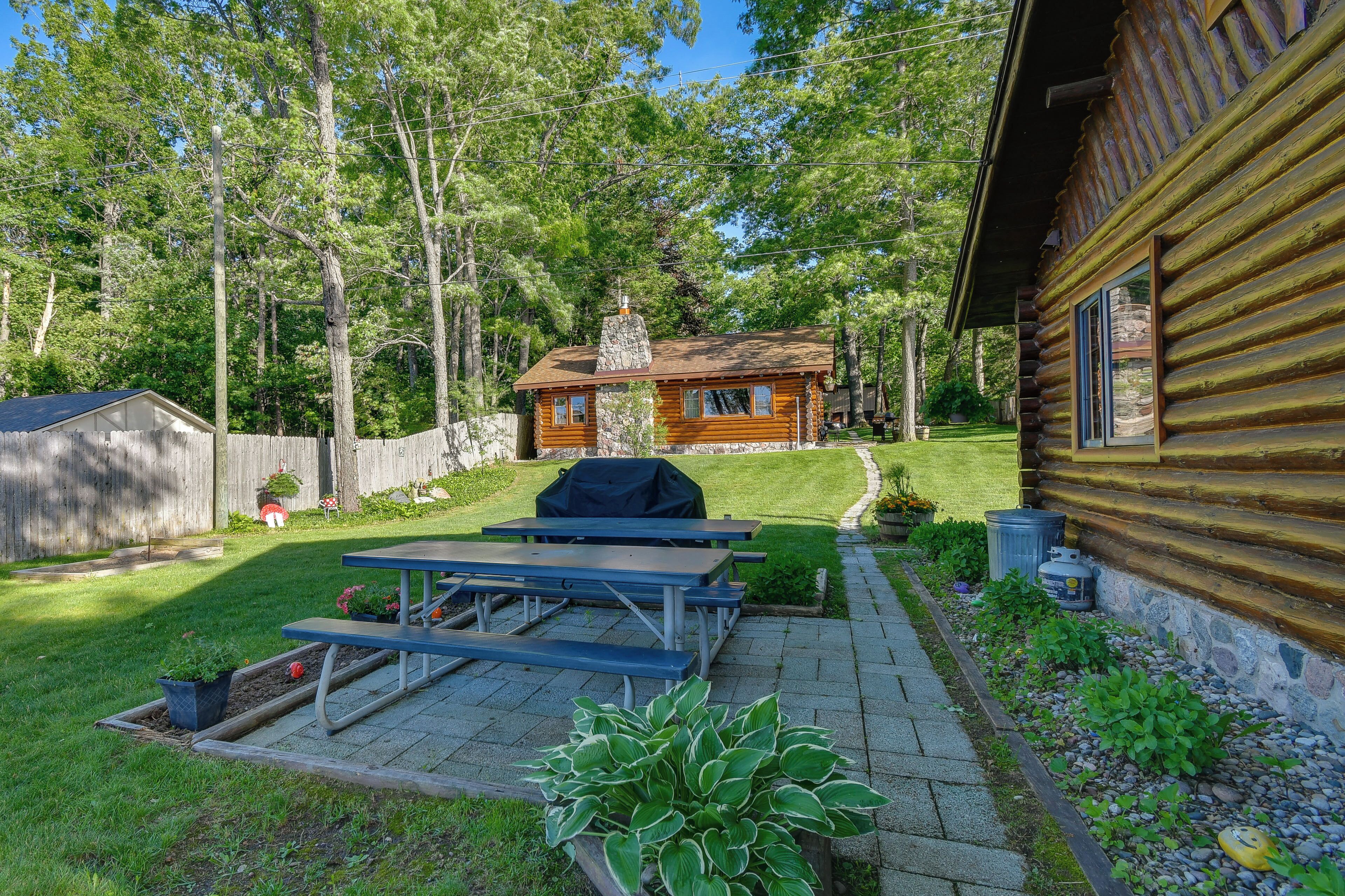 A wooden cabin with a picnic table and grill, surrounded by a well-maintained lawn and trees.