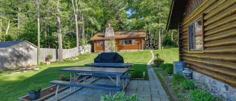A wooden cabin with a picnic table and grill, surrounded by a well-maintained lawn and trees.