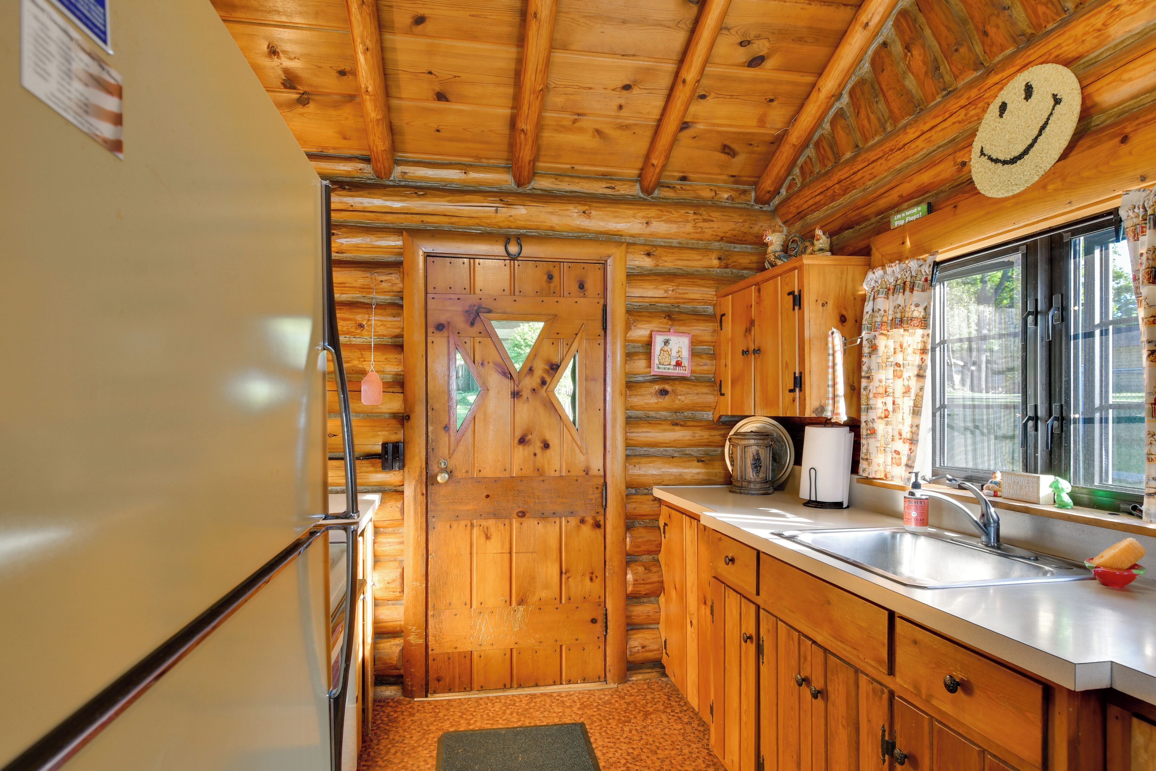 Interior de una cabaña de madera con cocina, que incluye un refrigerador, pileta y armarios de madera.