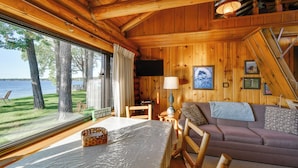 Una cabaña con interior de madera, un sofá, una mesa con una cesta, un televisor y vistas al lago.